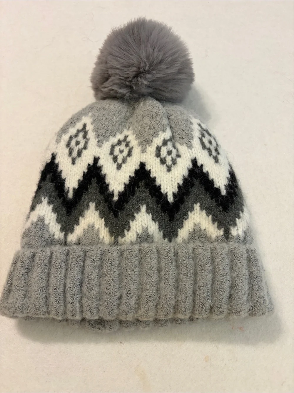 Gray knit beanie with a Fair Isle zigzag pattern and a fuzzy pom-pom on top.